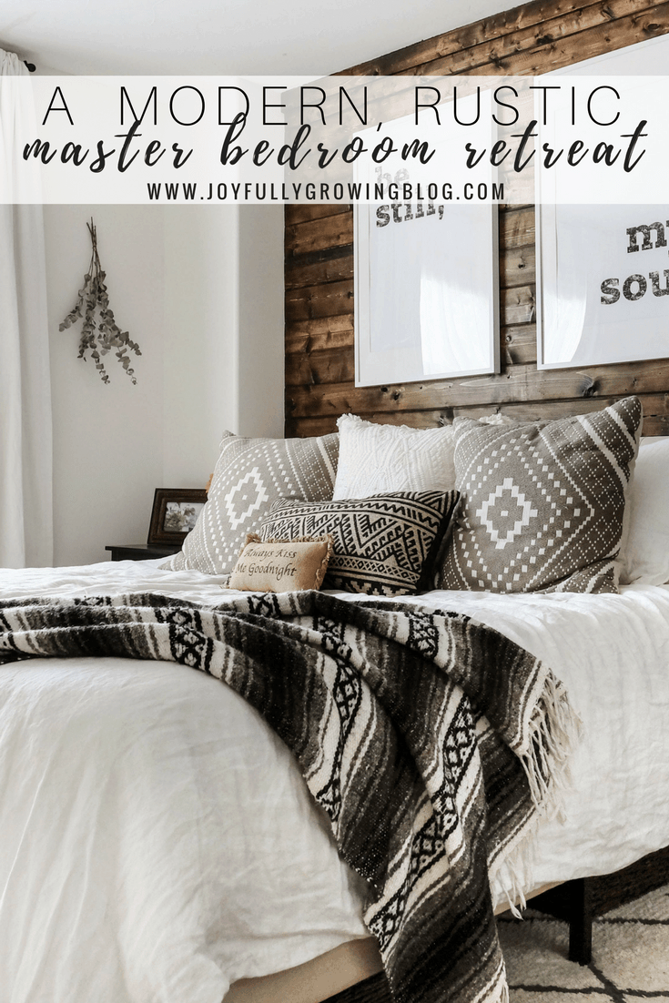 A rustic bedroom with a closeup of the bedding including throw pillows and blanket, up against a wood plank wall. Text overlay "A Modern, Rustic Master Bedroom Retreat - www.roomcrush.com"