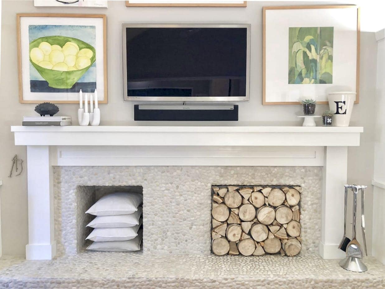 Fireplace mantle with art and TV hung above it and stacked logs in the fireplace insert