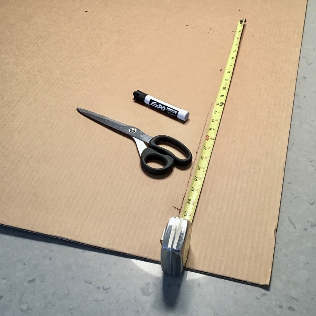 Flat cardboard with tape measure, scissors, and expo marker laying on top