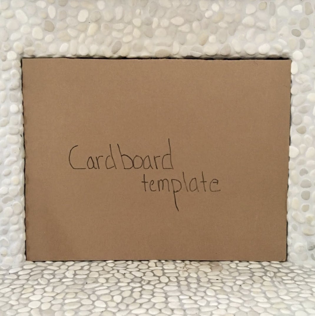 Square cardboard cutout inside of a fireplace opening with the words 'Cardboard template' written on it