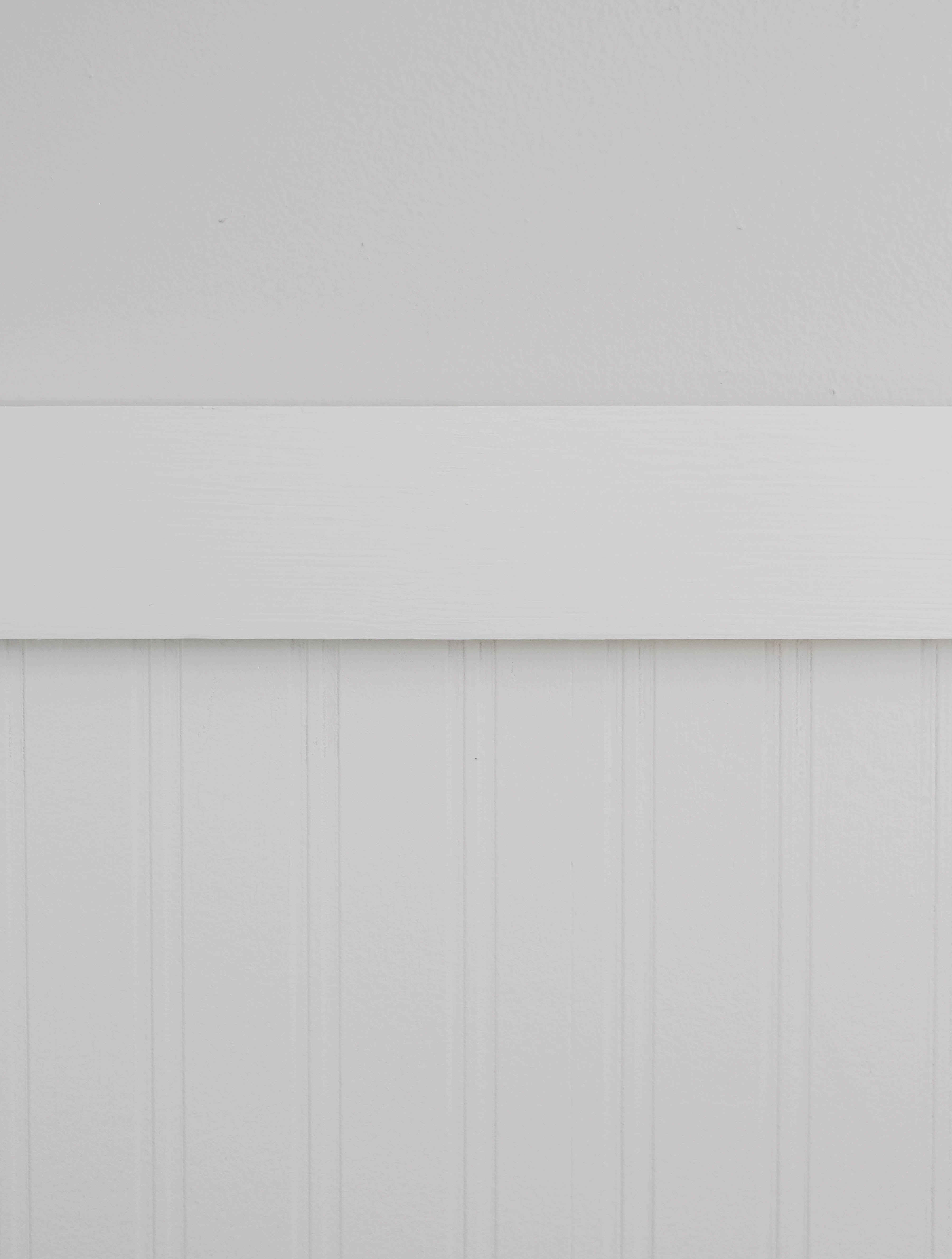 Closeup of white trim separating a light grey wall and white beadboard wallpaper