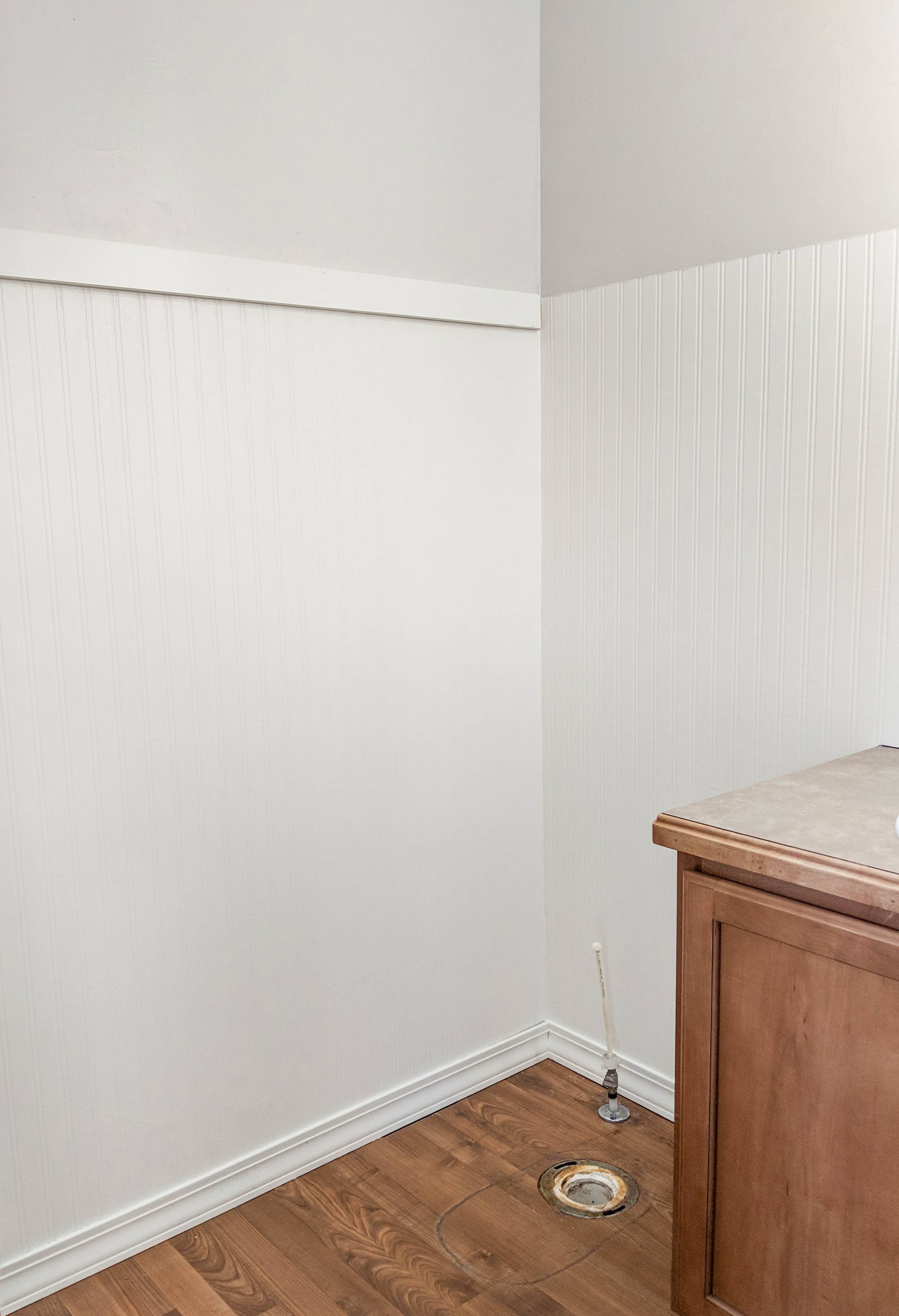 Corner of a small bathroom with toilet removed featuring white beadboard wallpaper