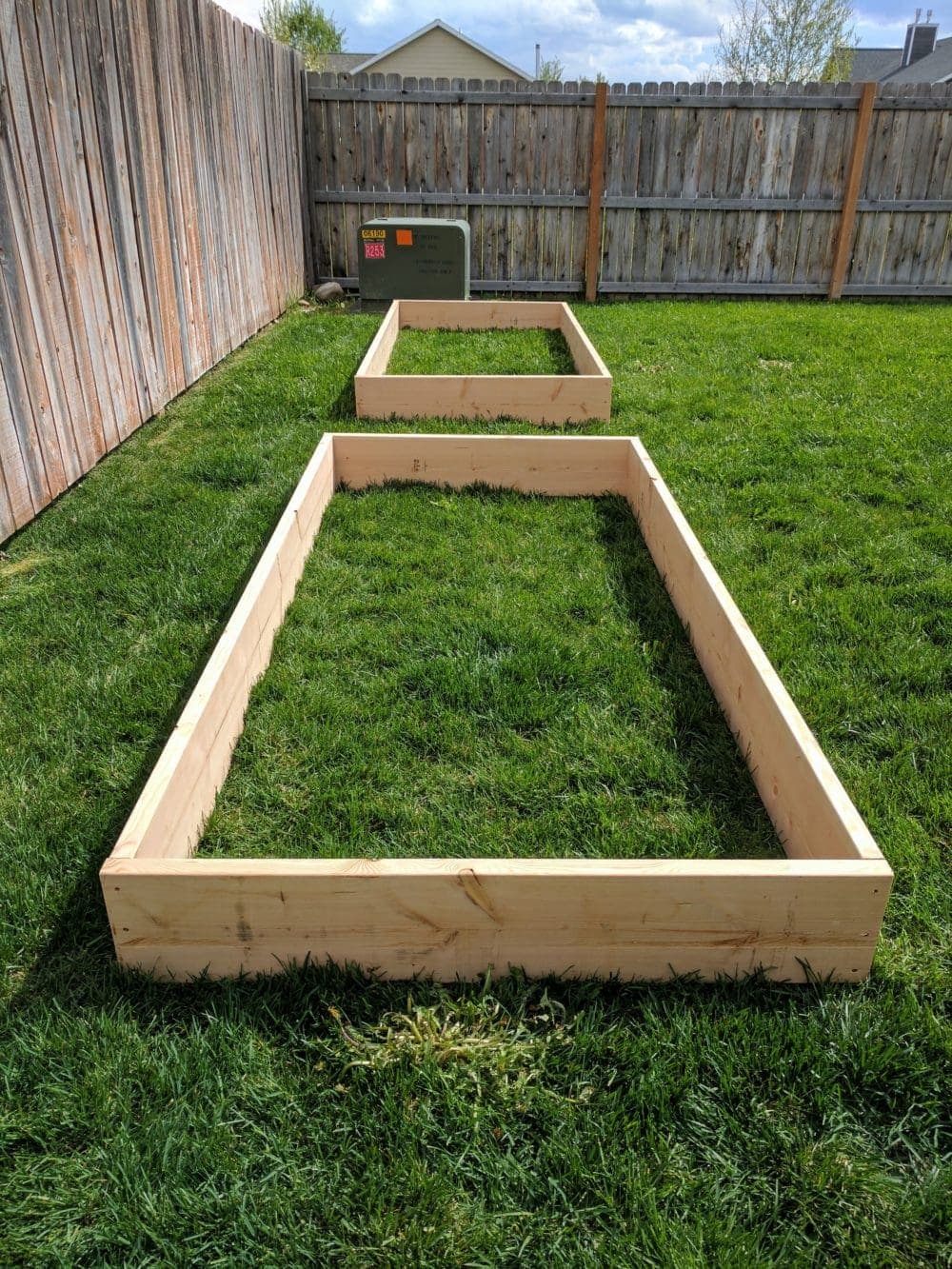 Two empty raised garden bed frames sitting in a grassy fenced yard