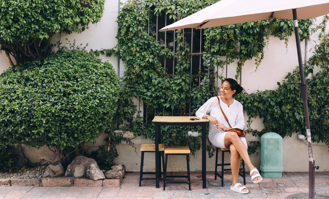 Woman sits in outdoor patio smiling as she learns about 4 Summer Decor Trends You Should Keep All Year Long