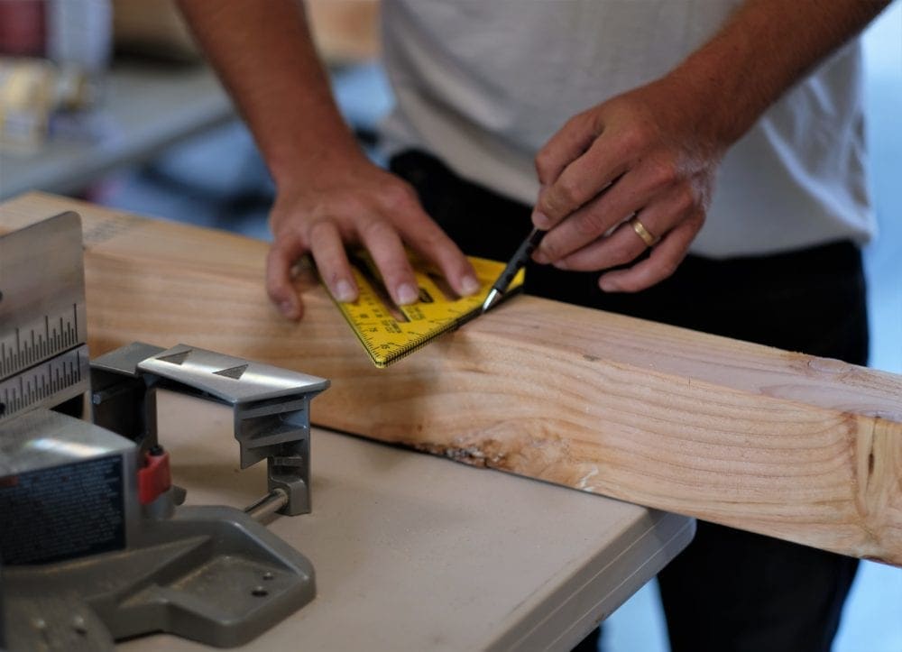 man marking a wood board with a speed square to make a rustic coffee table