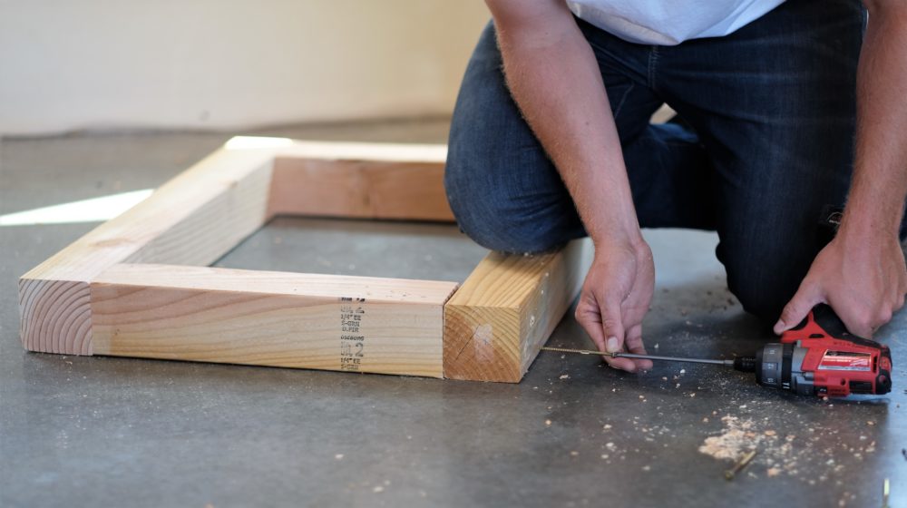 man using a drill to screw boards together for a rustic coffee table