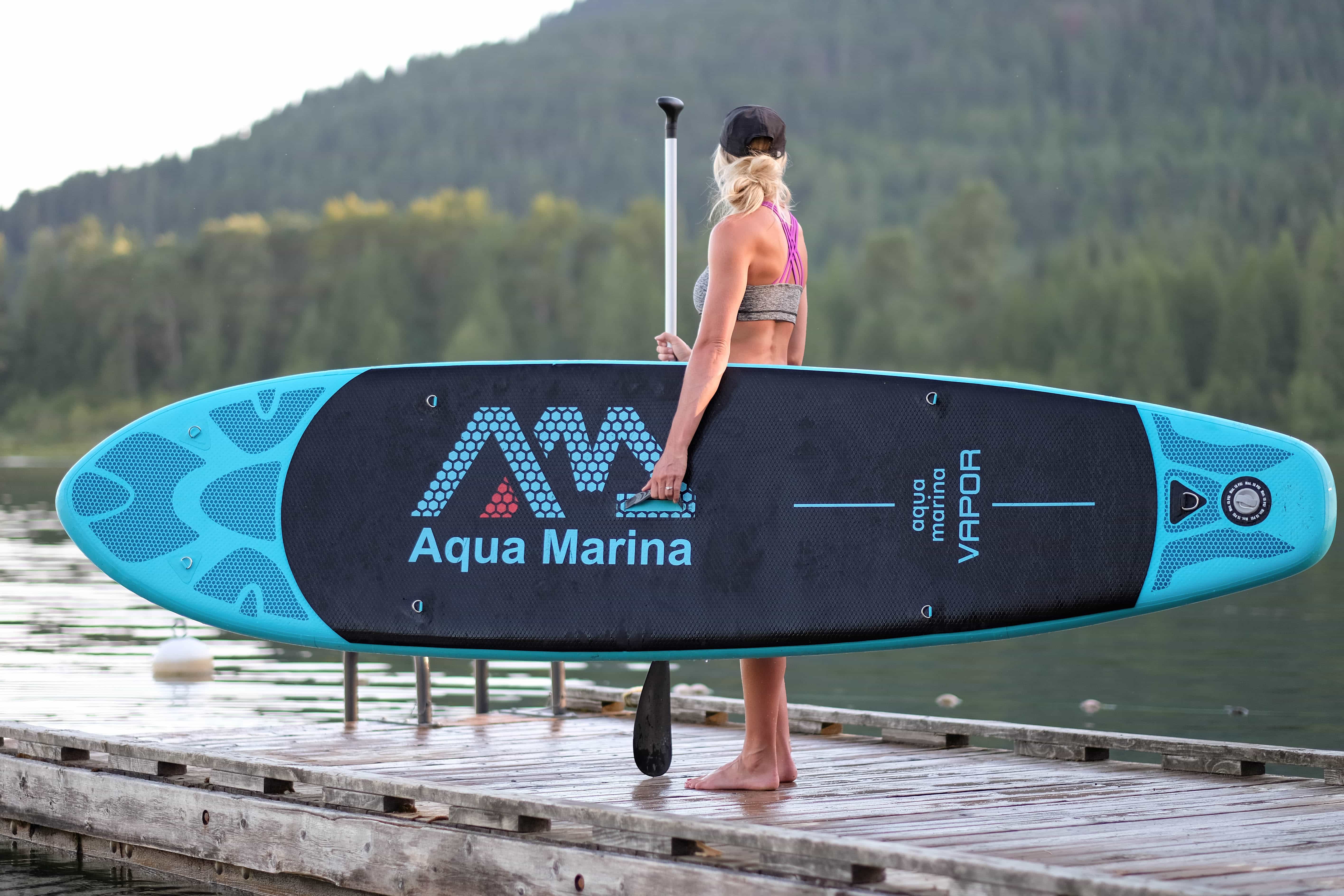 girl holding inflatable SUP standing on a dock looking over the lake