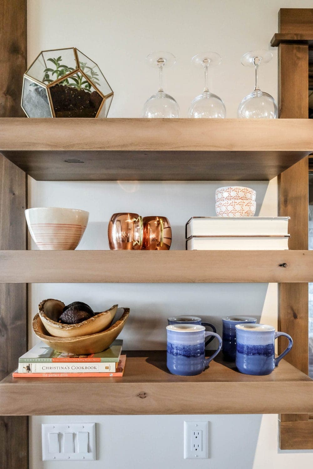 kitchen shelves styled with wine glasses, a bowl, books, and mugs