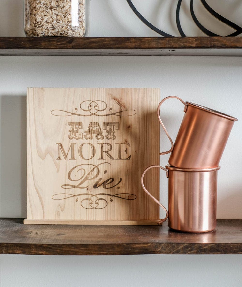 shelf styled with a Eat More Pie sign, and two stacked copper mugs