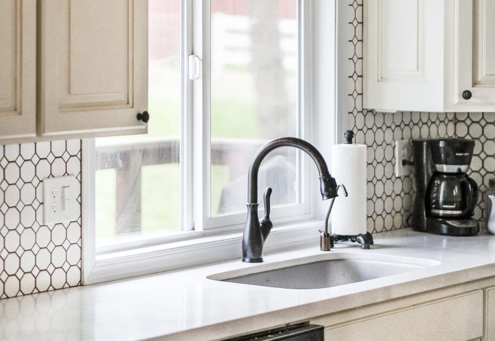 Farmhouse undermount stainless steel sink with goose neck faucet in front of a window