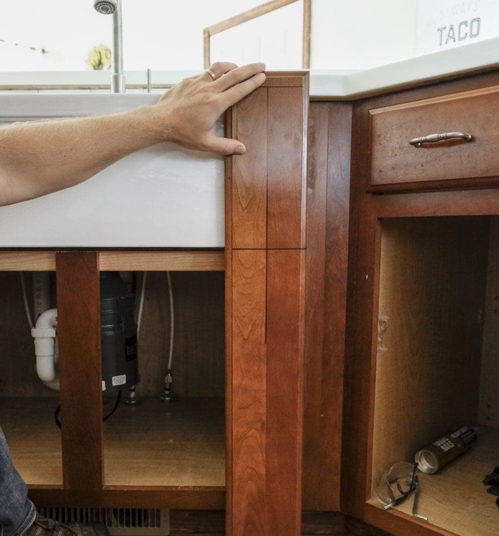 Holding old cabinet trim piece next to apron front farmhouse sink to show how to create new trim piece