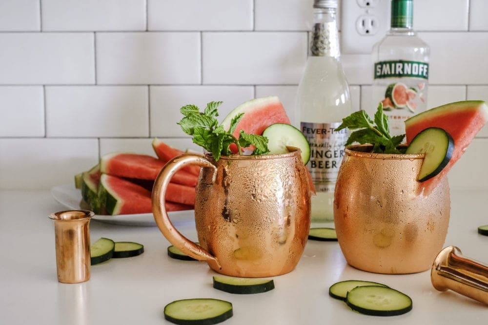 Two copper mugs with cucumber watermelon moscow mule ingredients