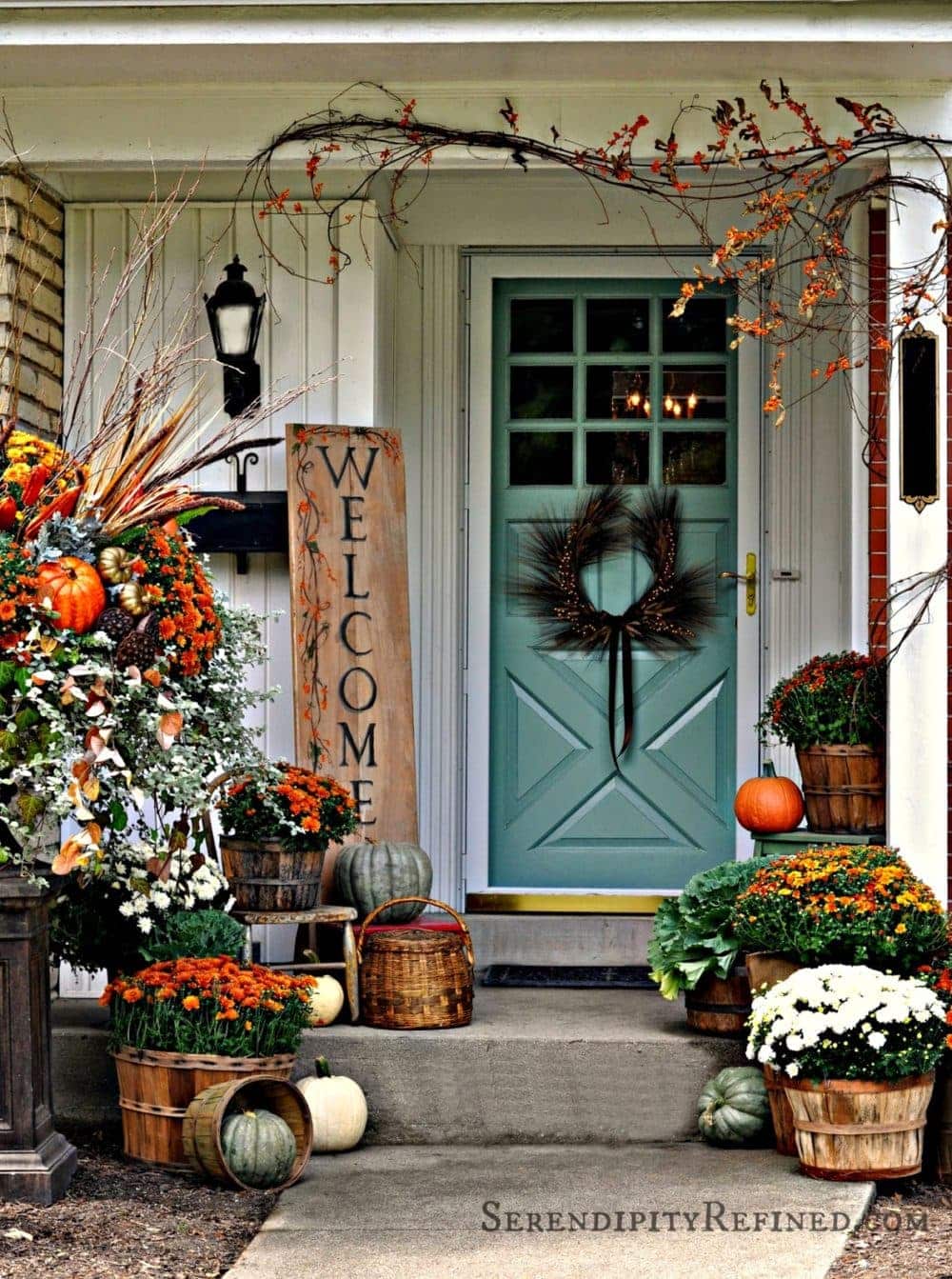 Fall front porch ideas using mums, pumpkins and branches draped over the door