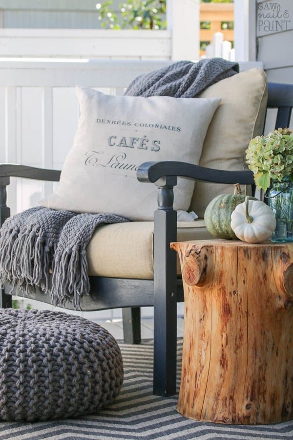 Fall front porch ideas using a blanket and throw pillow on a chair next to an old stump used as a side table