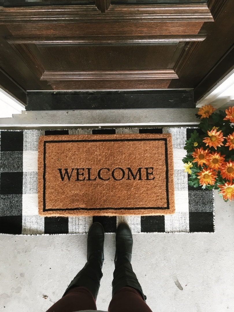 Fall front porch ideas with a jute welcome doormat layered over a black and white checkered doormat