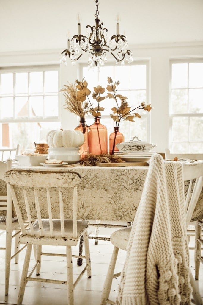 Thanksgiving table centerpieces with neutral linens and amber bottles filled with dried stems 