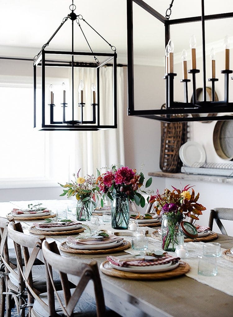 Thanksgiving table centerpieces with three blue vases filled with fall florals and eight place settings