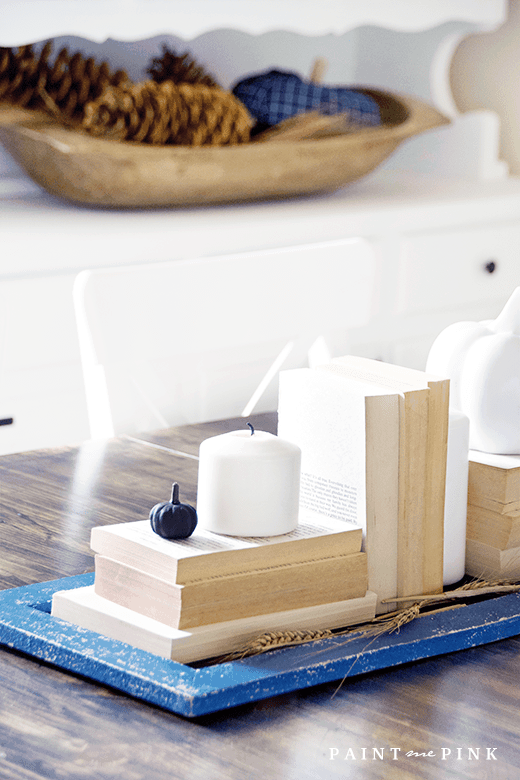 Thanksgiving table centerpieces with stacked vintage books and white candles on a blue runner