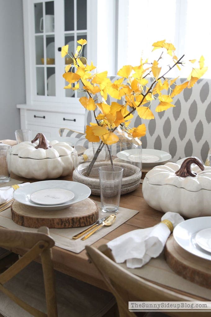 Thanksgiving table centerpieces with bright yellow leaves and white pumpkin casserole dishes