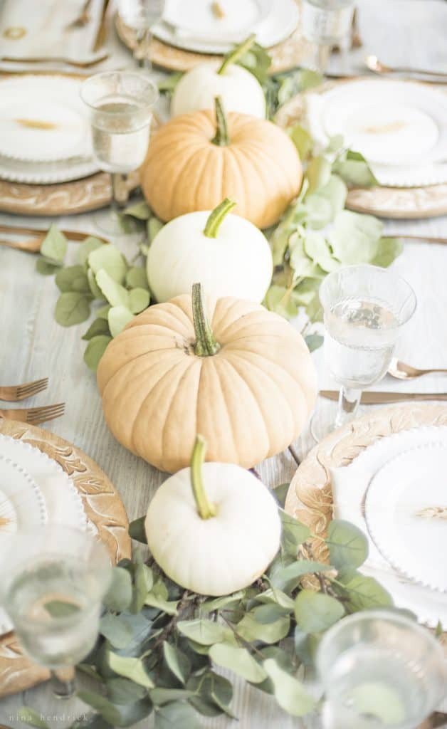 Thanksgiving table centerpieces with alternating orange and white pumpkins on a eucalyptus runner