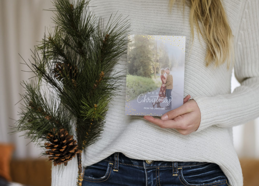 Woman holding a Christmas card photo and a pine tree branch