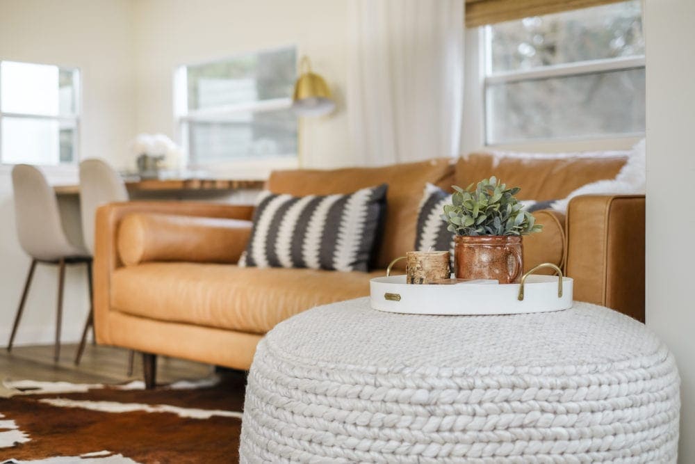 Closeup of a fabric floor pouf with a tray on top in front of sofa