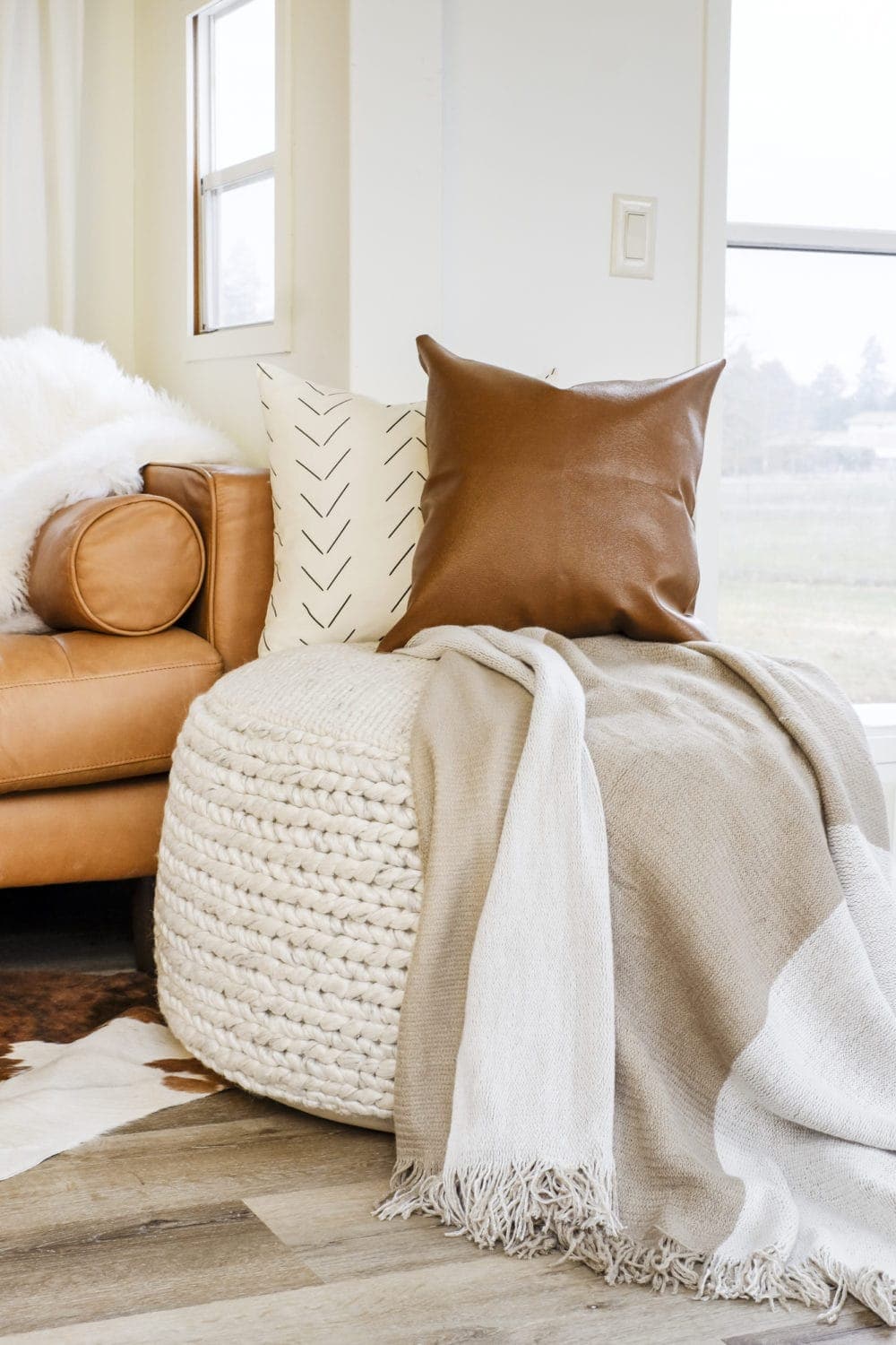 Large fabric pouf with two throw pillows and a blanket on top