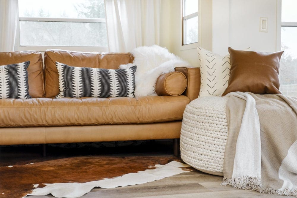 Large woven pouf in front of a leather sofa with pillows and a blanket