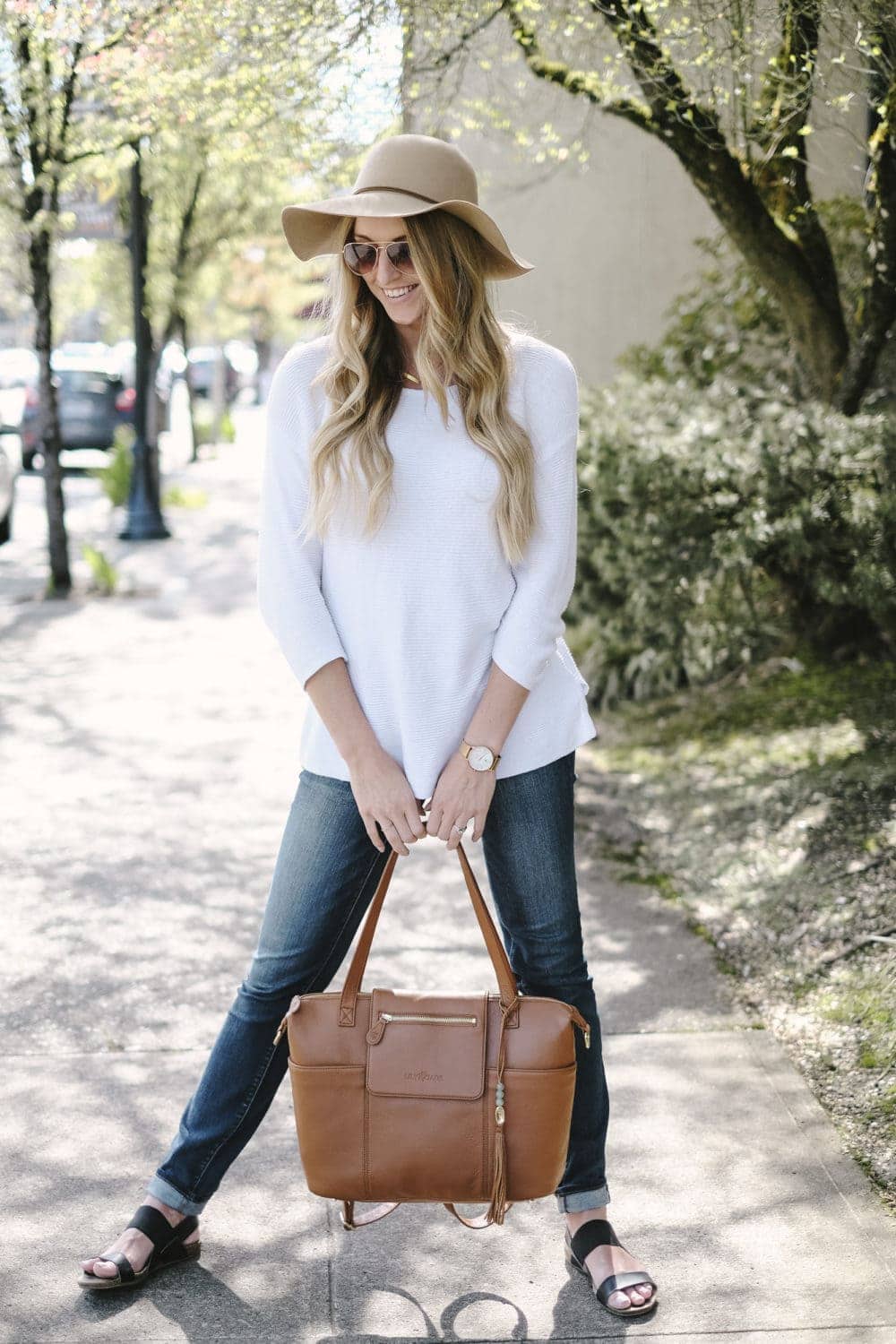 diaper bag review featuring a blonde woman holding leather bag on sidewalk