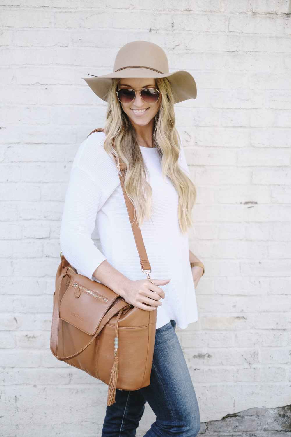 blonde woman carrying leather diaper bag with messenger strap on shoulder