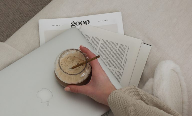 hand reaches for iced coffee while she reads the best Coffee Gift Ideas For Caffeine Lovers